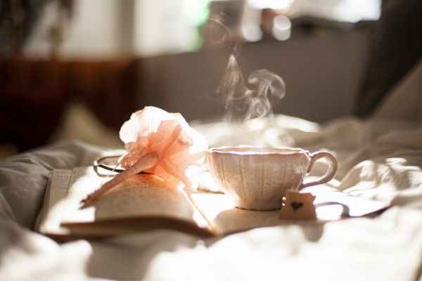 Steaming teacup, carnation, and book laying on a bed